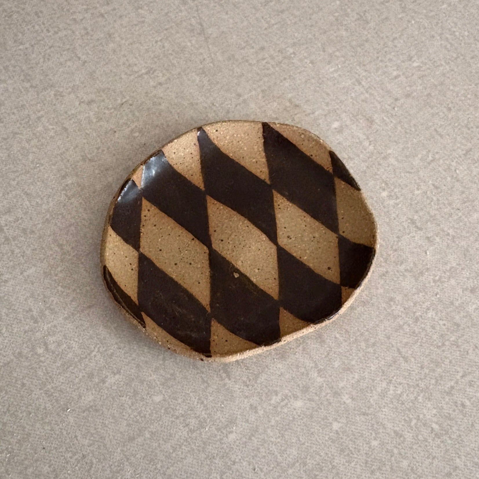 Round ceramic stone with black and beige diamond pattern on a beige background